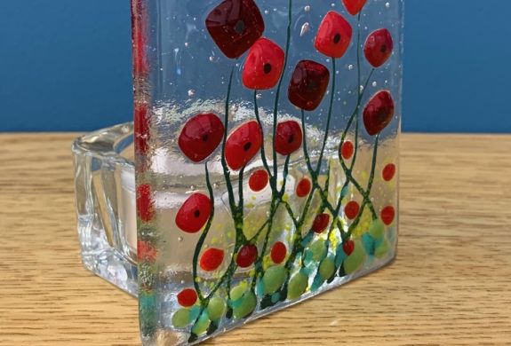 a tealight holder made of clear fused glass with a red poppy design
