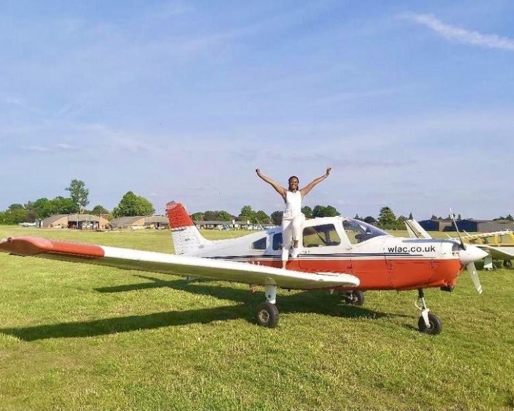Woman standing on the wing of an aeroplane posing for a photo after a having a pilot lesson