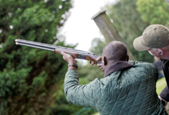 man pointing shotgun to the sky with instructor looking on as part of clay pigeon shooting experience