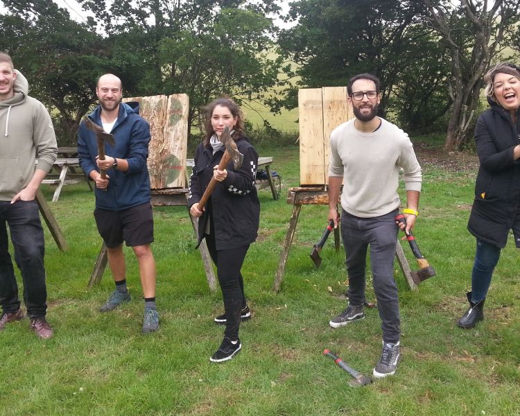 five people standing in a line in front of wooden boards holding axes for a photo as part of an axe throwing experience