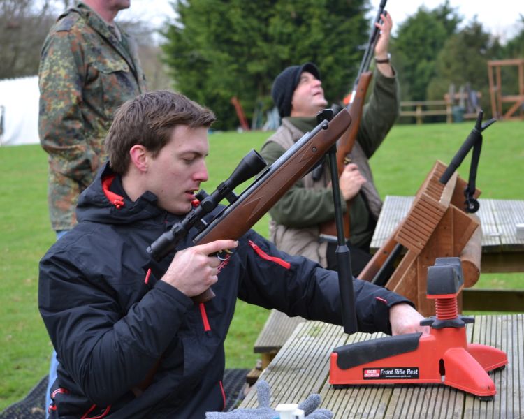 man sitting at table outside holding an air rifle as part of an air rifle shooting experience with instructor in background
