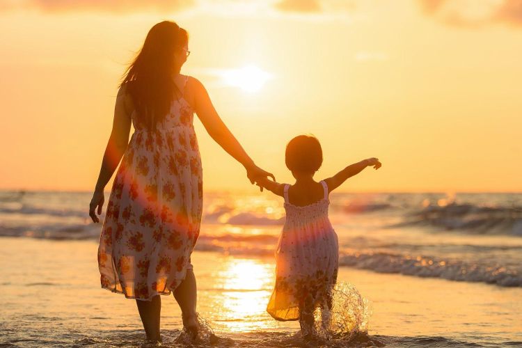Mum walking on beach with young child at sunset