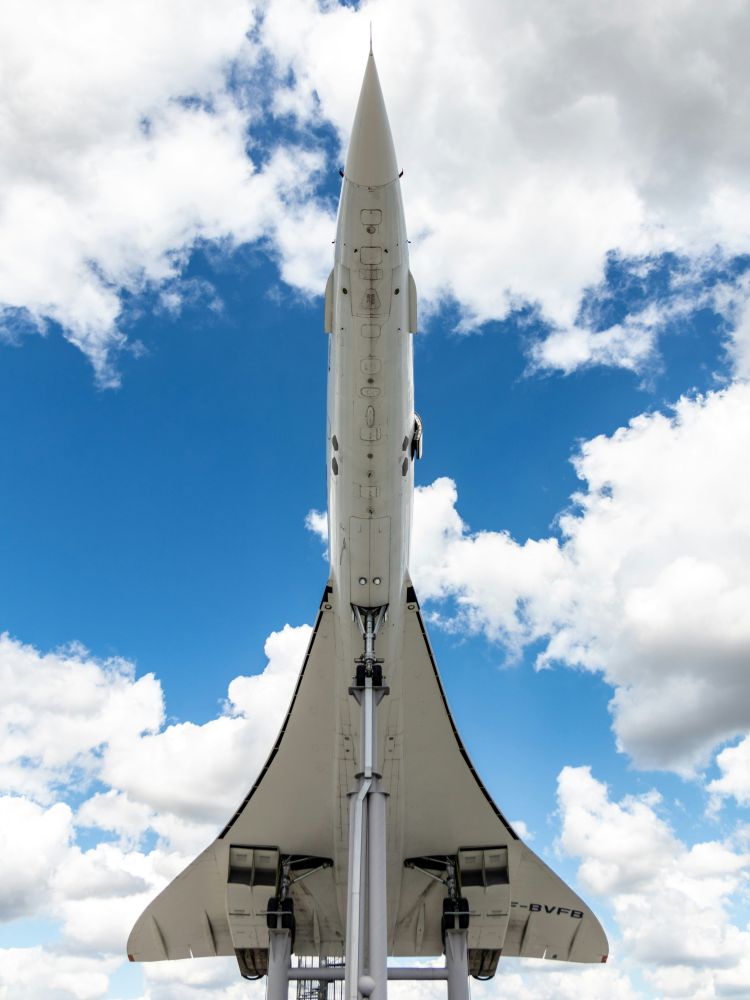 The underside of the concorde plane against a blue cloudy sky