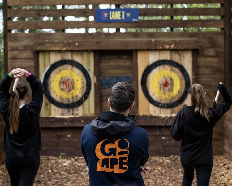 two girls throwing axes watched by instructor at go ape axe throwing experience