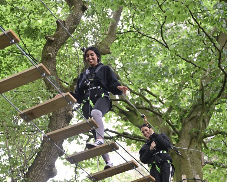 two girls walking the rope bridge on treetop adventure plus course at go ape