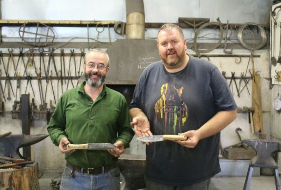 Two men holding knives they have made on a blacksmith experience day