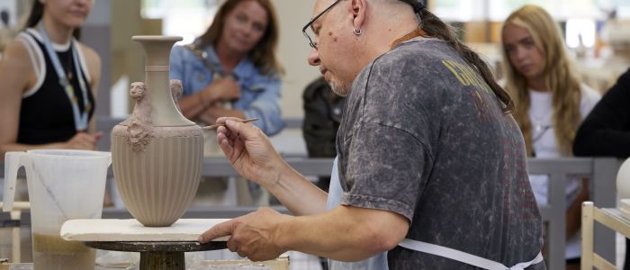 people watching a man decorate a vase on the wedgwood factory tour