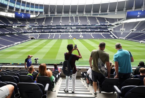 visitors in the stands overlooking the pitch on the tottenham hotspur stadium tour in london
