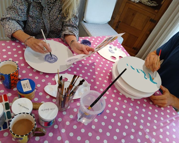 people sitting at a table painting ceramic plates