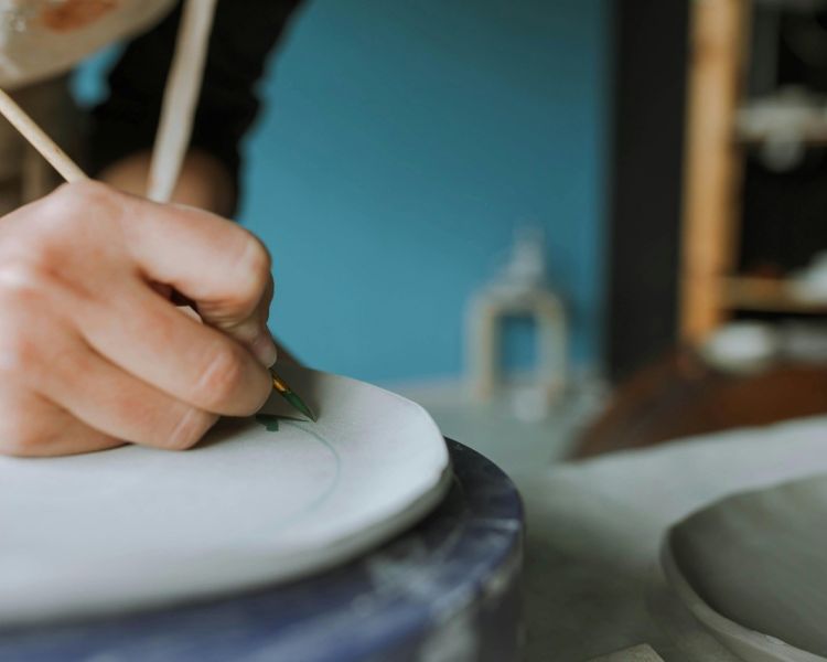 person painting with a fine brush on a ceramic plate