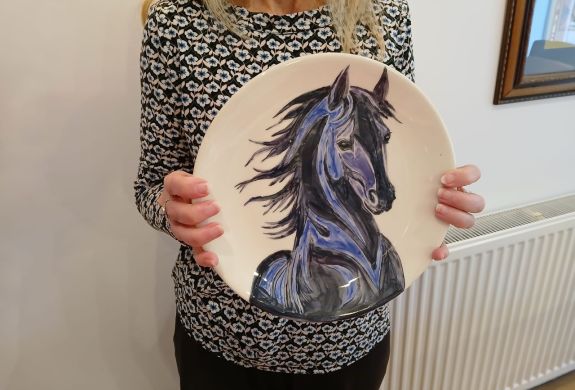 lady holding a plate with a horses head painted on it