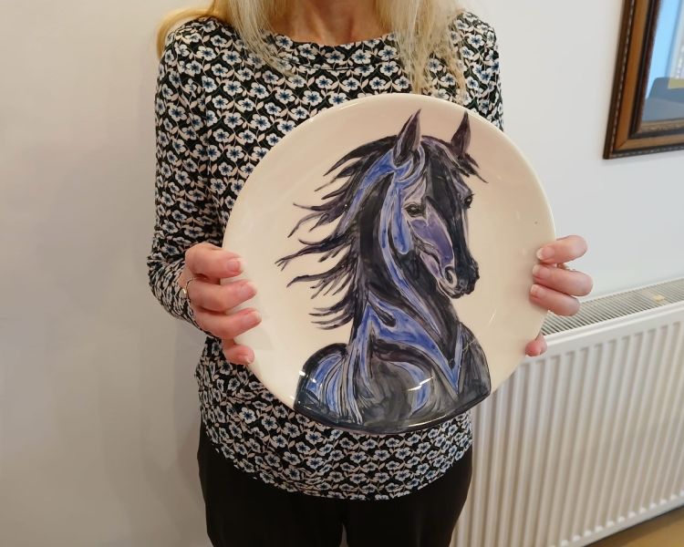 lady holding a plate with a horses head painted on it