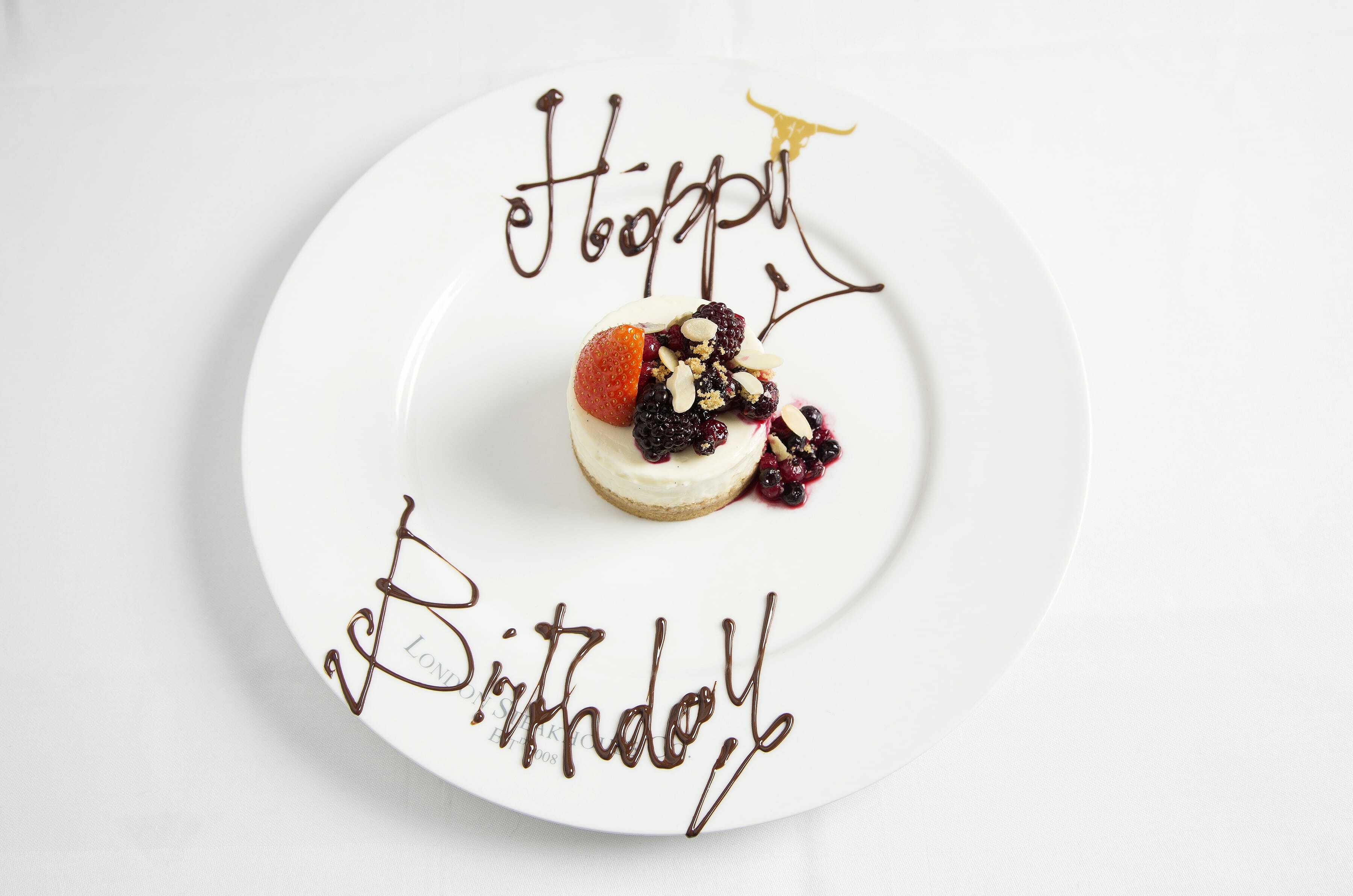 a white plate with a small dessert in the middle and happy birthday written in chocolate around it at the london steakhouse co