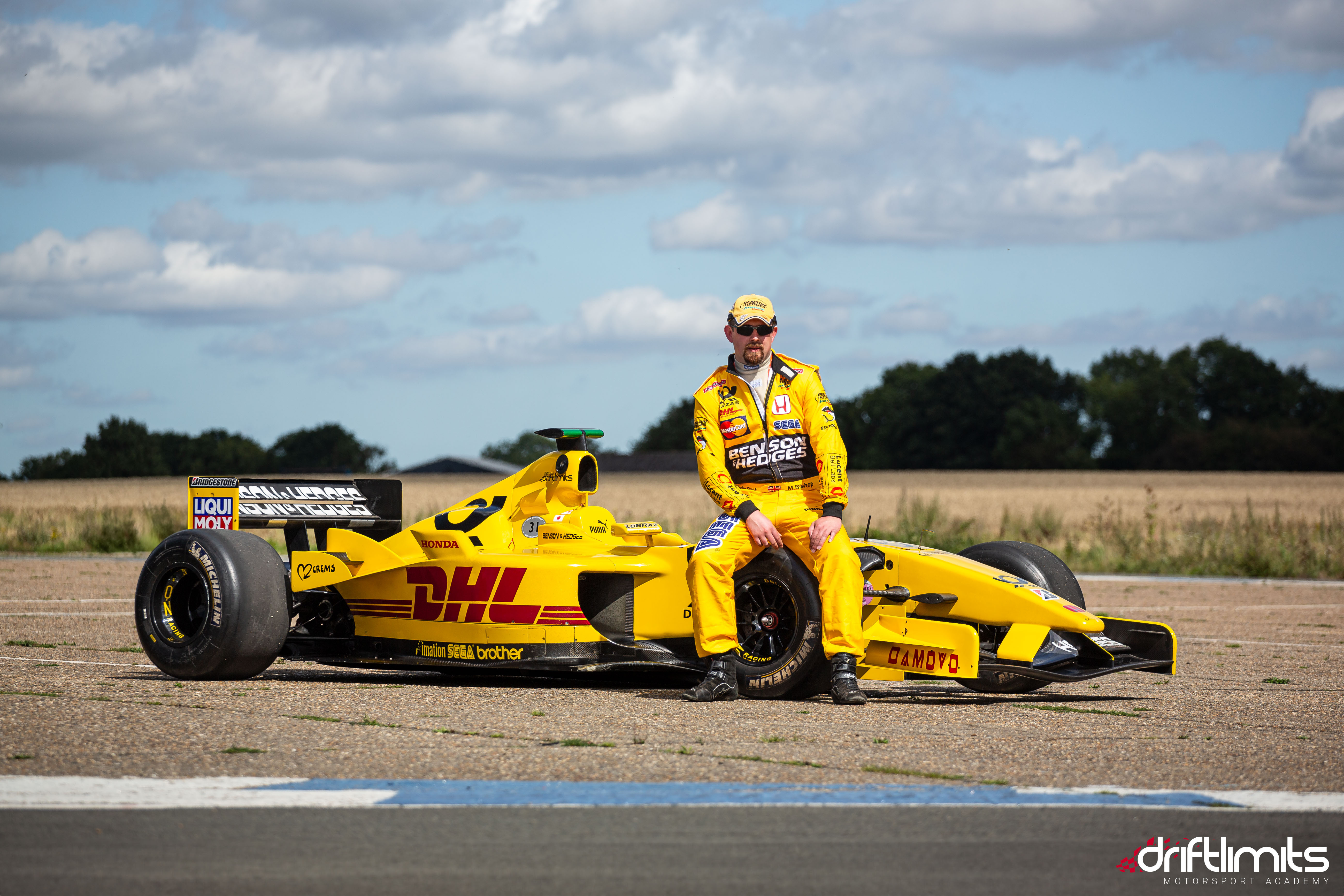 man in yellow driving suit sat on an f1 jordan car on a f1 car photoshoot and passenger lap experience