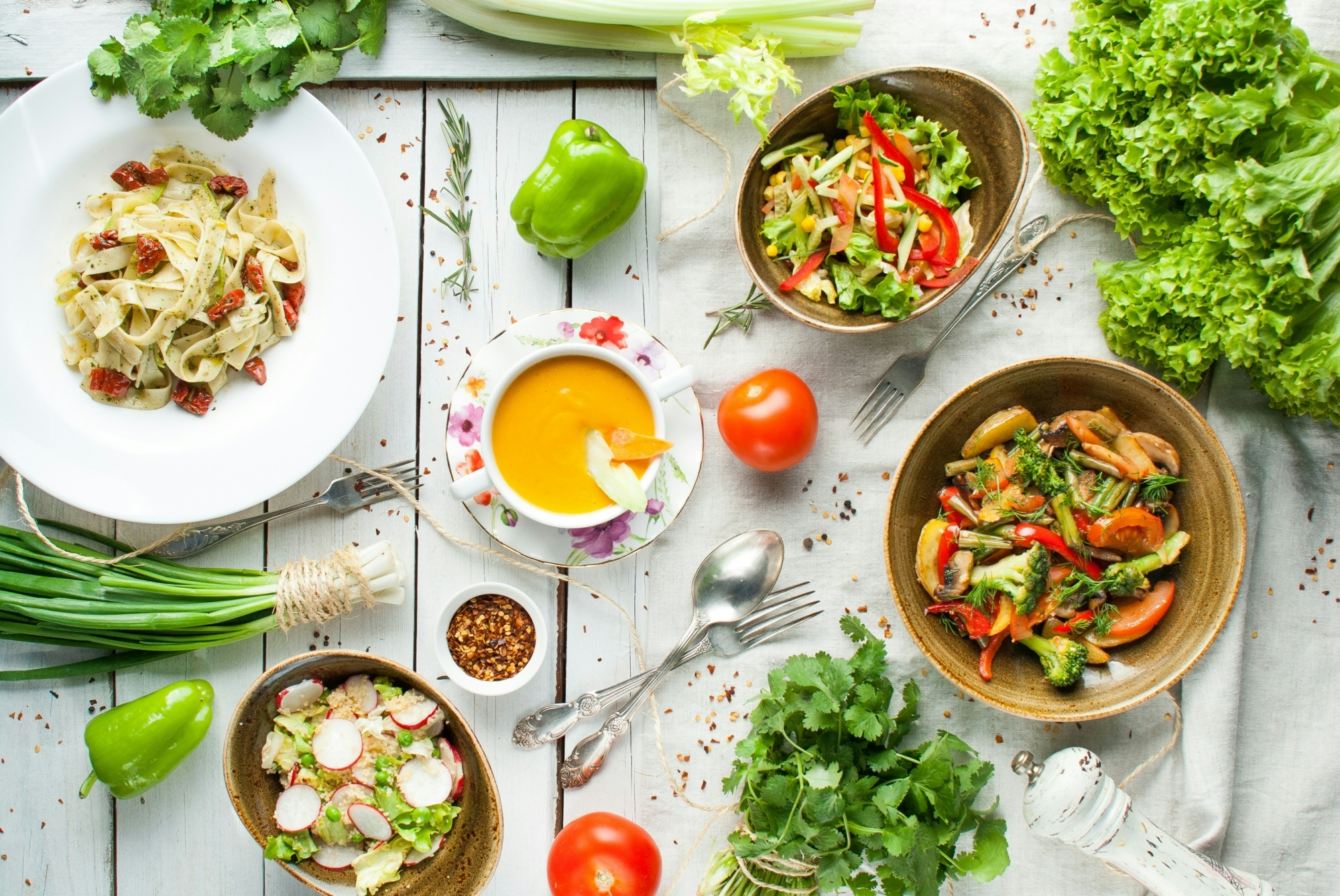 colourful food dishes surrounded by vegetables on a white wooden table