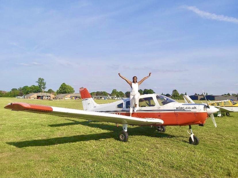 Woman standing on the wing of an aeroplane posing for a photo after a having a pilot lesson